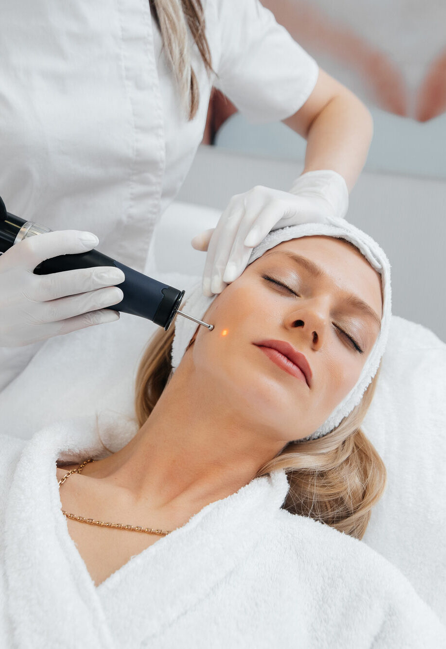 A young girl gets a charcoal peeling for the skin of the face in a beauty salon. Laser pulses cleanse the skin. Hardware cosmetology. The process of photothermolysis, warming the skin.