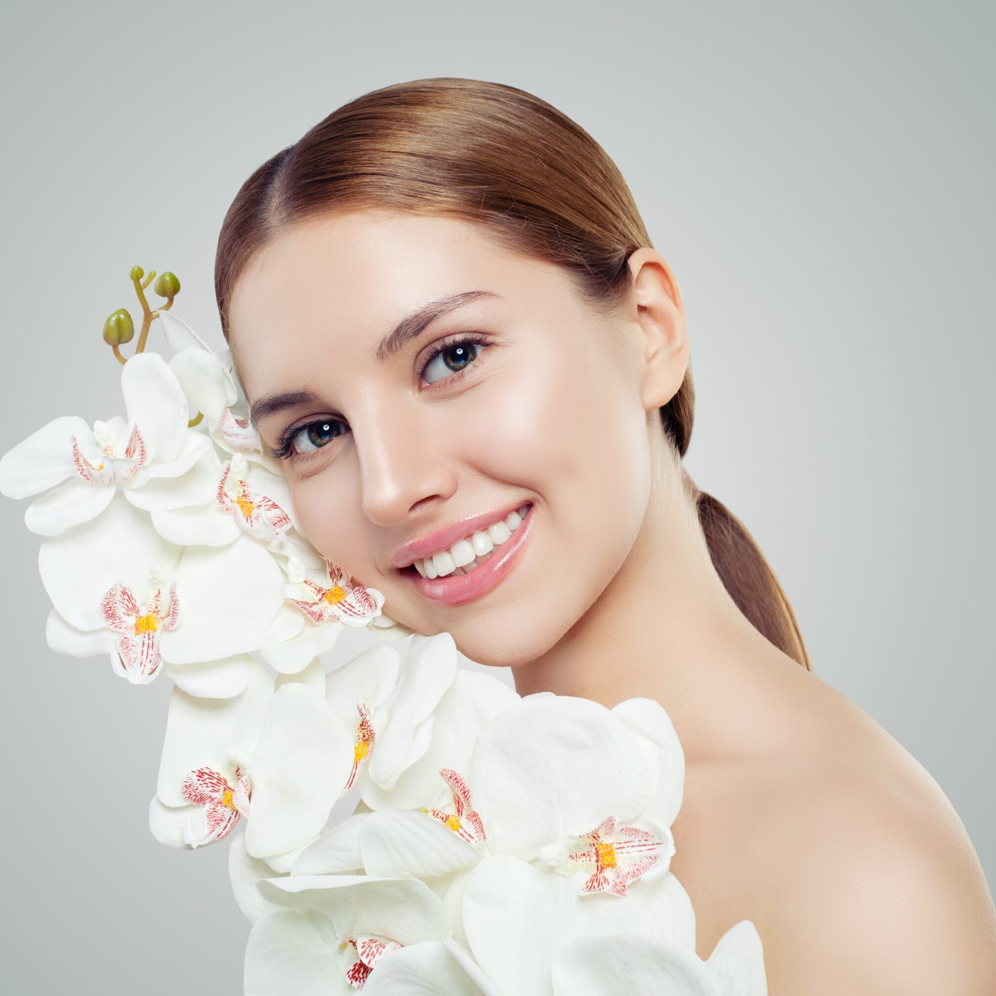 Young smiling woman with healthy skin and white orchid flowers. Skincare, spa beauty, cosmetology and facial treatment concept