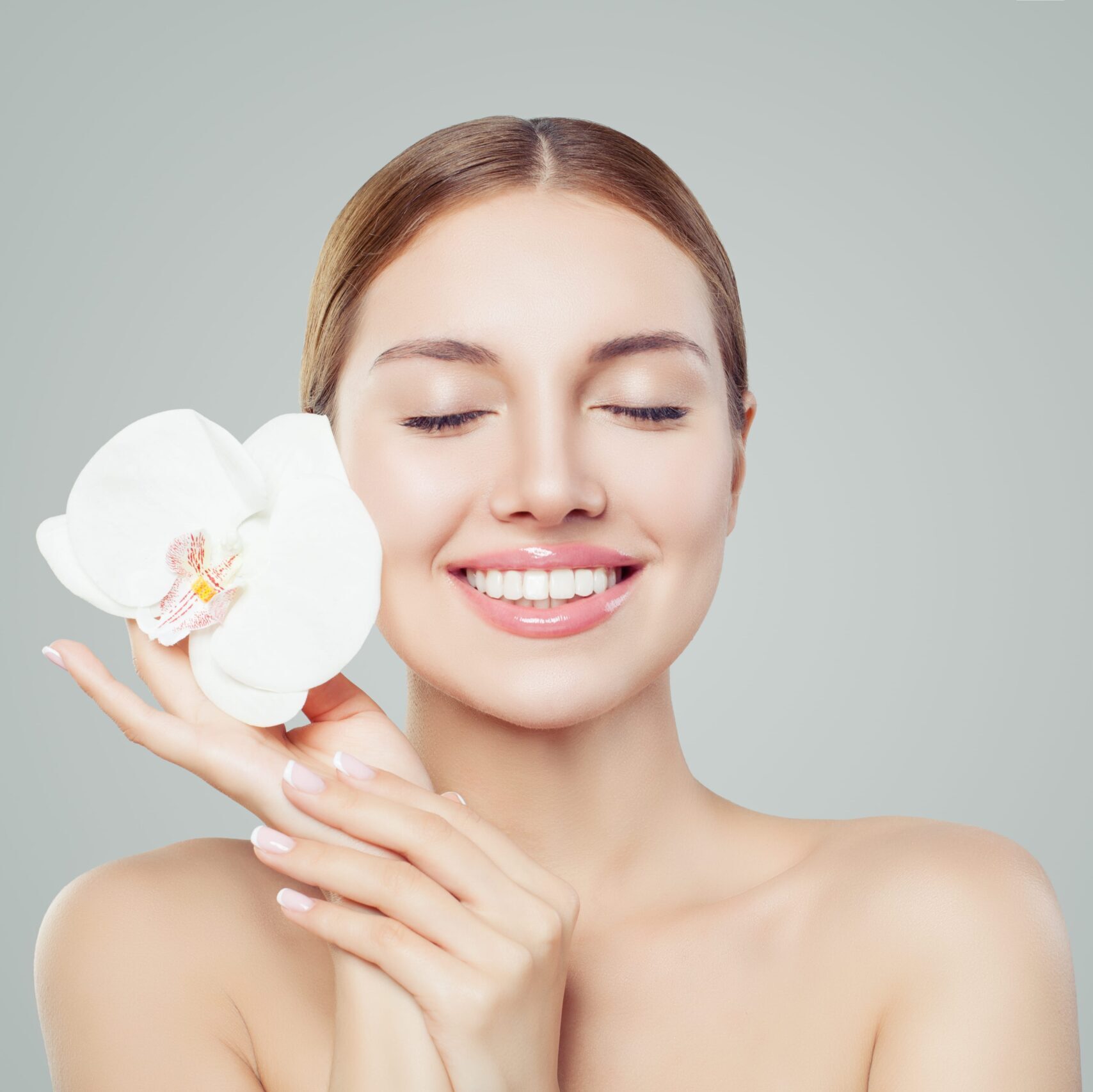 Beautiful smiling woman with healthy skin, cute smile and orchid flower on white background. Spa, skincare, facial treatment and wellness concept