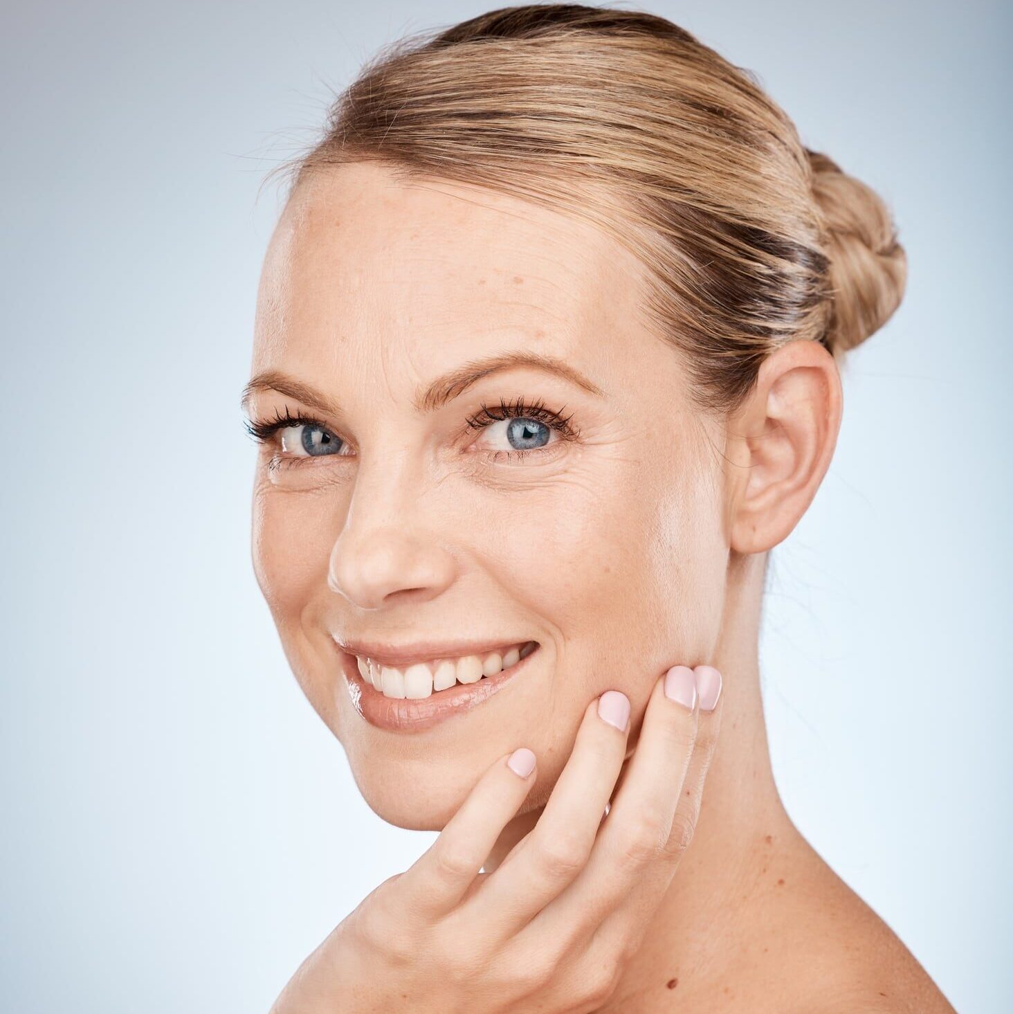Beauty, skincare and woman with hand on face for natural cosmetics, healthy skin and cosmetic dermatology. Portrait of happy wellness model, organic facial glow and smile on a gray studio background.